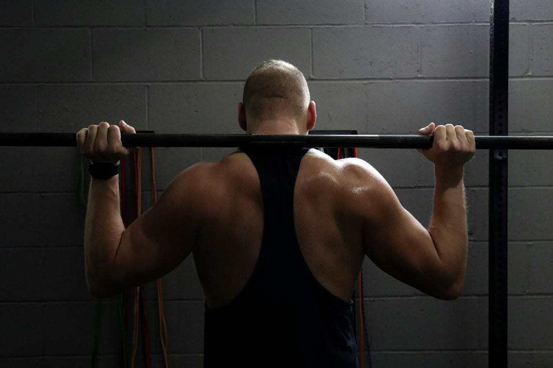 Close-up of a man's back doing pull-ups in a dark, moody gym with concrete walls